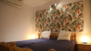 A bedroom with a bed, wooden headboard, nightstand, and a wall with a tropical bird and plant pattern. - T2 apartment Beachfront (Banyuls-Sur-Mer)