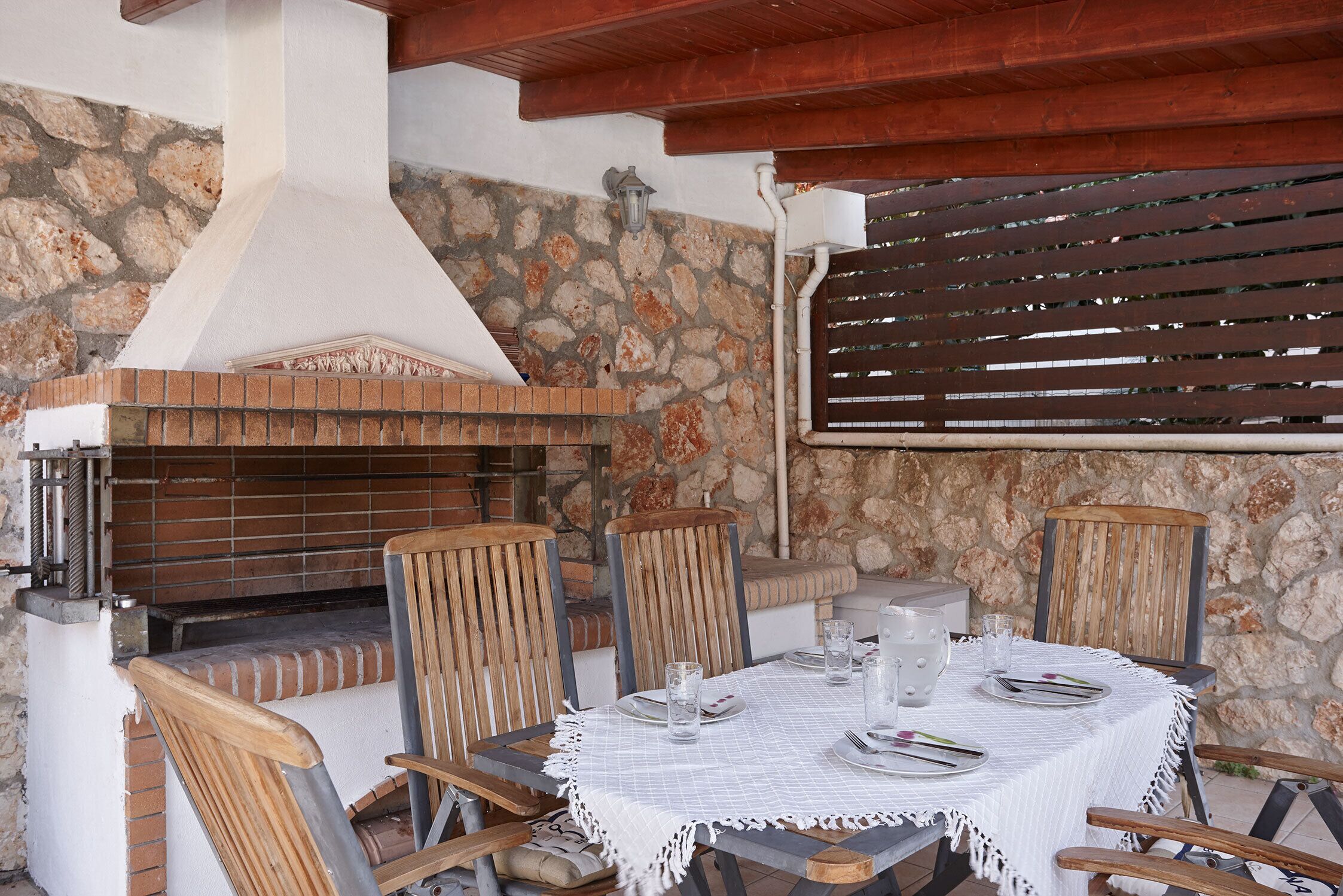 An outdoor dining area with a stone wall, wooden chairs, and a table set for four.