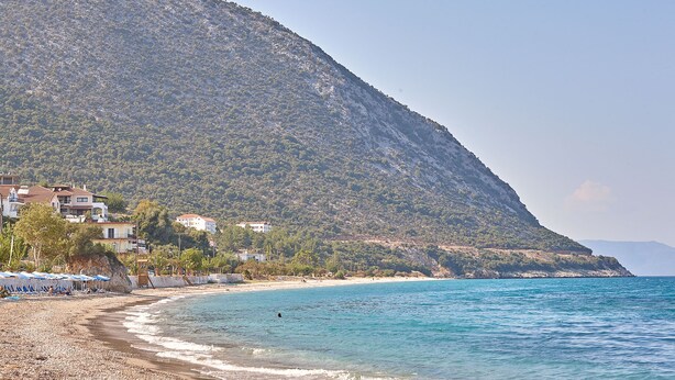 Una platja amb un litoral rocos, alguns paraigües i edificis damunt d'una vessant.