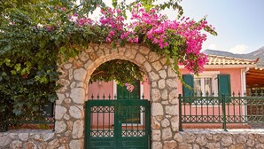 Un arc de pedra amb una porta verda, que condueix a un edifici amb façana rosa i persianes verdes.
