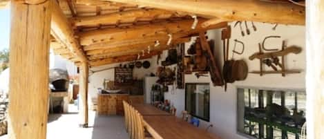 A rustic wooden interior with a long bench, wooden beams overhead, and various kitchen utensils hanging on the wall.