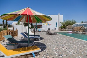 A poolside area with lounge chairs, a colorful umbrella, and a clear blue sky.