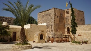 Un bâtiment historique, avec un palmier au premier plan, des murs en pierre et de grands vases.