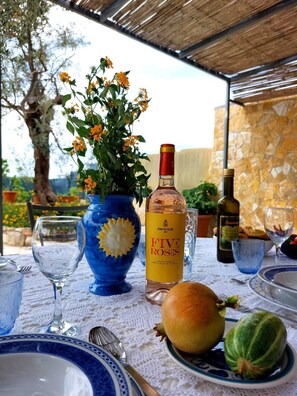 A table set for dining with a bottle of wine, a vase with flowers, and a pomegranate.