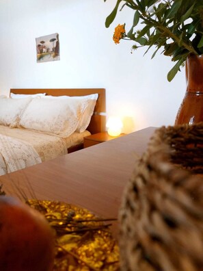 A bedroom with a wooden bed, white linens, a bedside table with a lamp, and a potted plant with orange flowers.