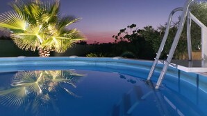 Una piscina con escalera, rodeada de palmeras y un cielo al atardecer.