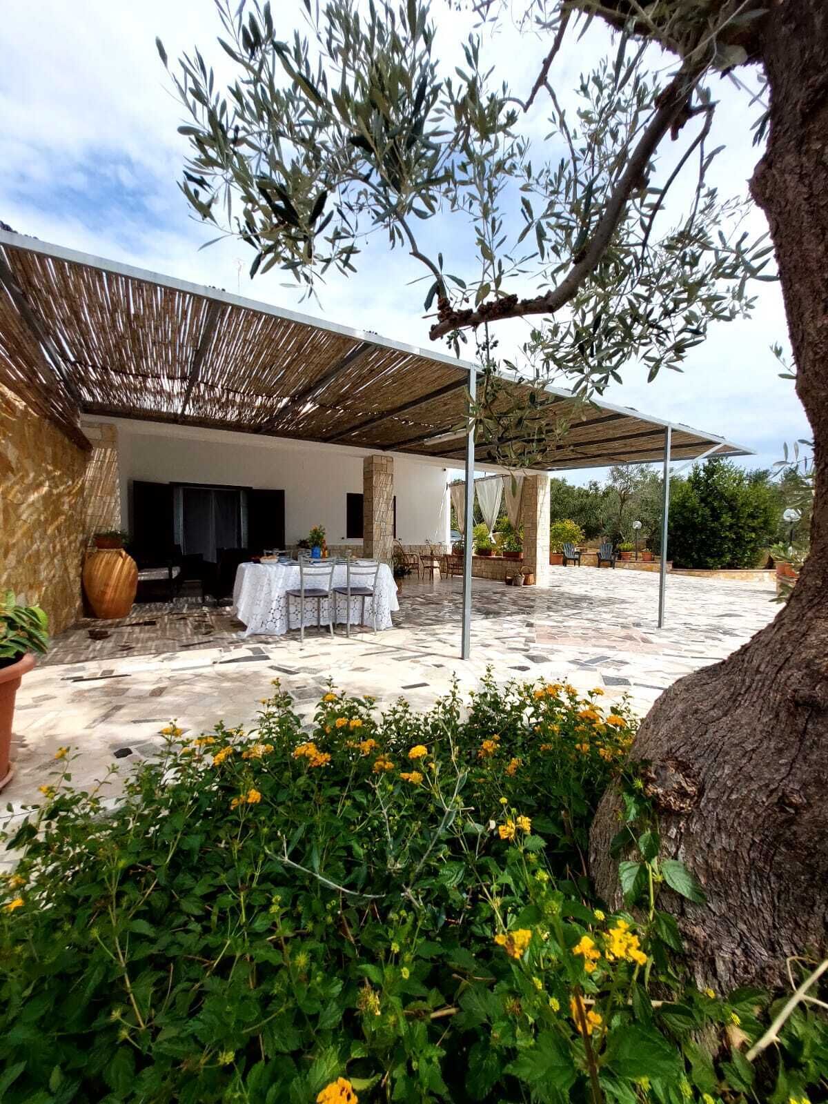Un'area patio esterna con un angolo relax coperto, pavimento in pietra e vegetazione circostante.