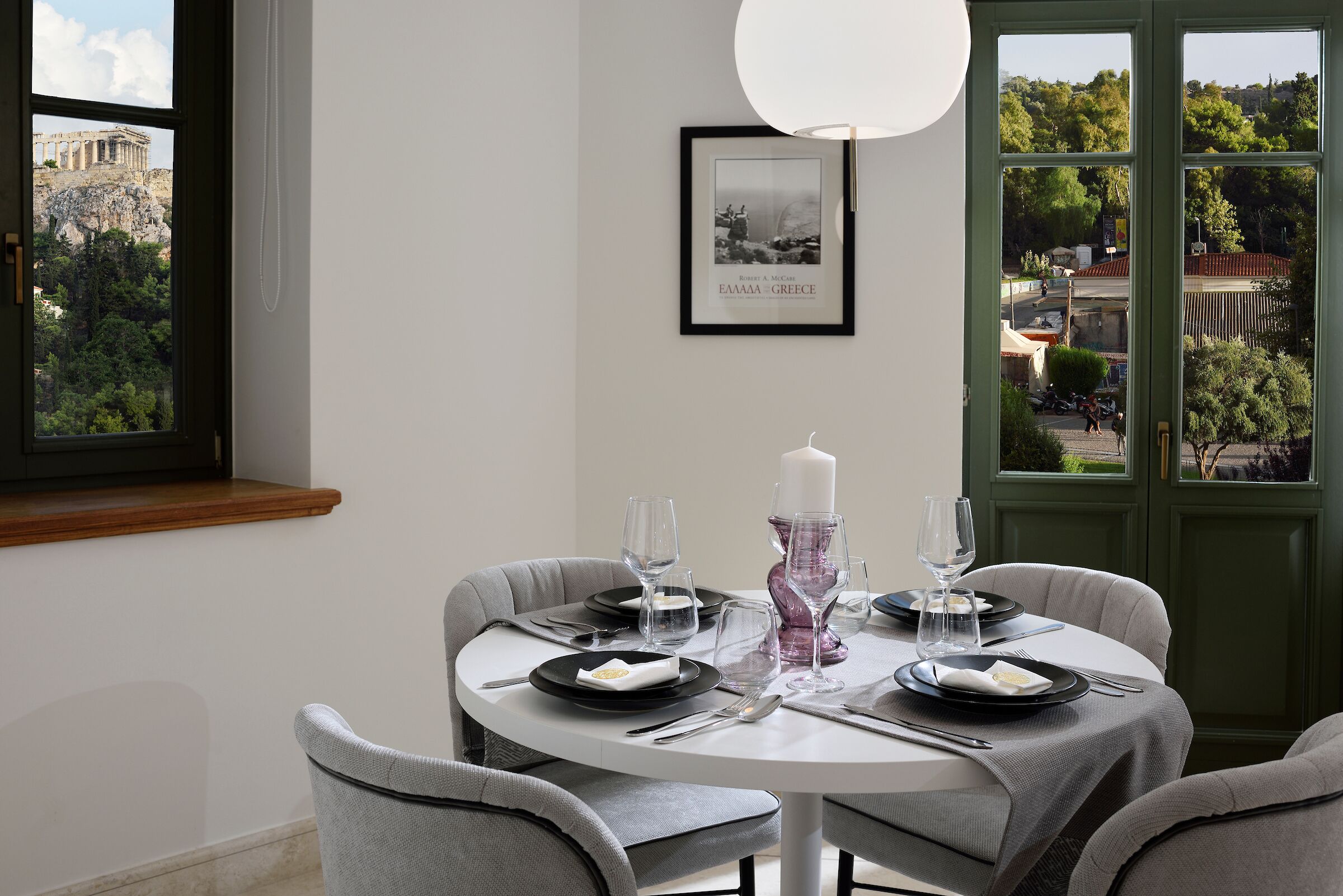 A dining area with a round table set for four, a framed picture on the wall, and a view of a historical building outside.