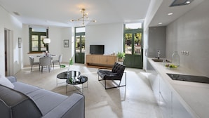 Ein modernes Wohnzimmer mit Sofa, Esstisch mit Stühlen, Fernseher und Küchenzeile mit Spüle und Arbeitsplatte.