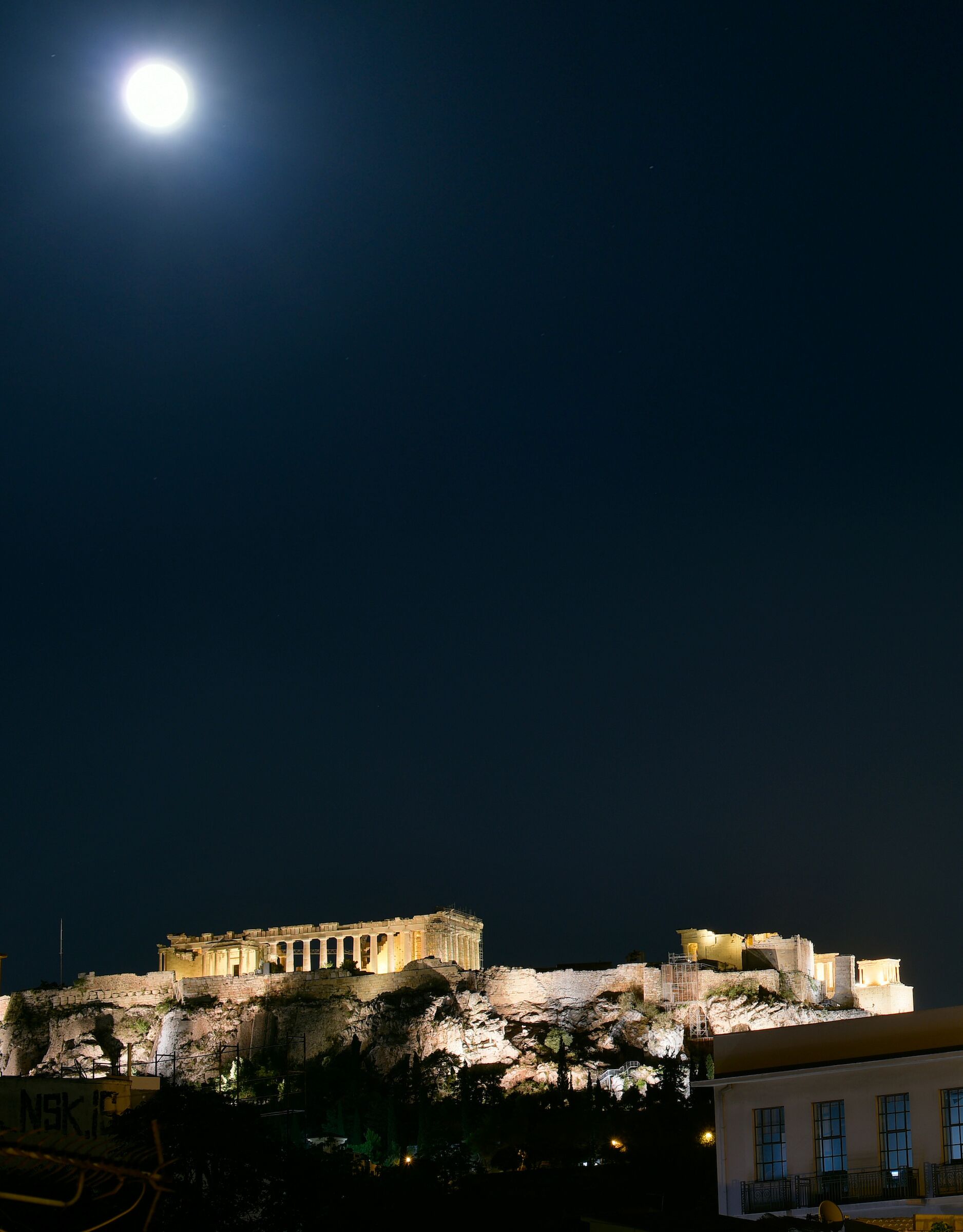 A historic building with classical architecture, illuminated at night, and a full moon in the sky.
