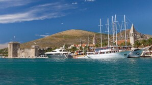 A coastal town with a historic tower, a large sailing ship docked at the harbor, and a hill in the background. - Apartment Karlo 2 - with Pool, 70m from sea (Okrug Gornji)