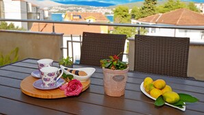 A balcony with a table set for tea, featuring a floral teacup, a rose, and a potted plant. - Apartment Karlo 2 - with Pool, 70m from sea (Okrug Gornji)