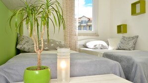 A hotel room with a bed, a bedside table with a green pot and a candle, and a window with a view of buildings. - Apartment Karlo 2 - with Pool, 70m from sea (Okrug Gornji)