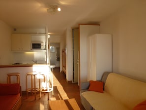 A compact living space with a kitchenette, a sofa, and a dining area with stools.