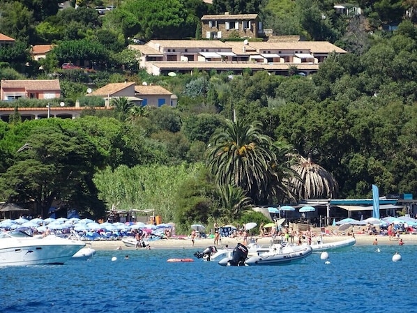 A coastal area with boats, beach umbrellas, and a building with a tiled roof.