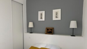 Ein Schlafzimmer mit einem Bett, zwei Kissen, einem Nachttisch, einer Lampe und zwei gerahmten Bildern an der Wand.