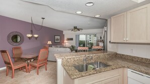 A modern kitchen with granite countertops, a built-in sink, and wooden cabinets. - Oceanwalk 2BR with Fountain Views Private Balcony and 5 Min Walk to Beach (New Smyrna Beach)