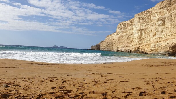 Una playa arenosa con olas rompiendo contra un acantilado.