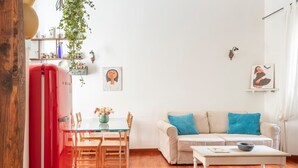 Uma sala de estar ampla com piso de madeira, uma mesa de jantar com cadeiras, um sofá com almofadas e uma mesa de centro.