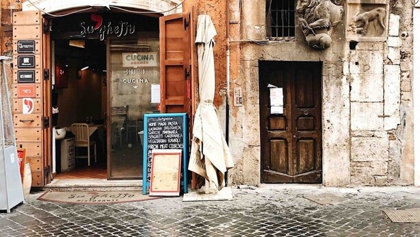Restaurante com fachada rústica, porta de madeira e placa indicando os itens do cardápio.