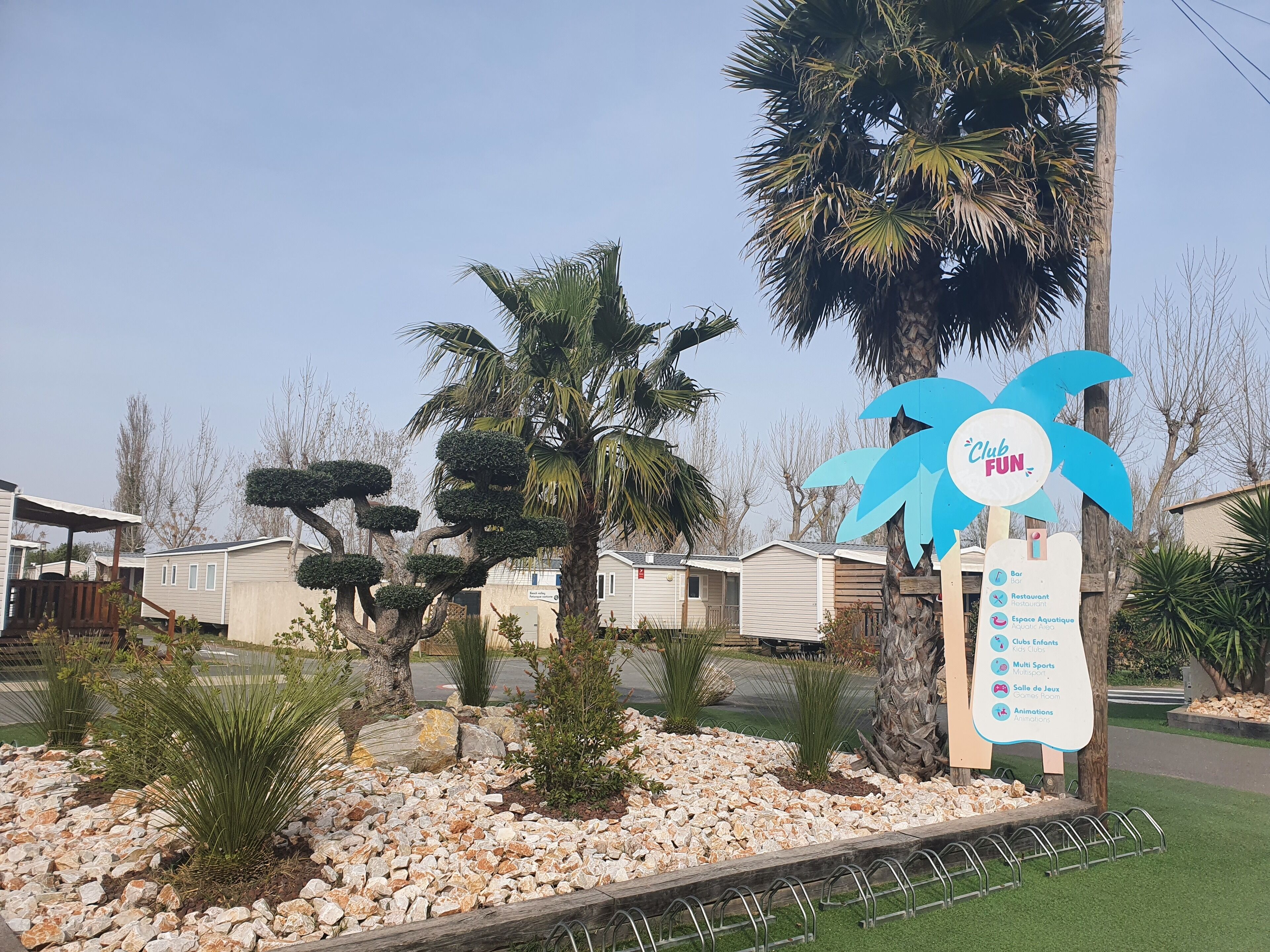 Une enseigne pour le Club Fun, indiquant les équipements disponibles, entourée de palmiers et d’un espace paysager agrémenté de rochers et de plantes.