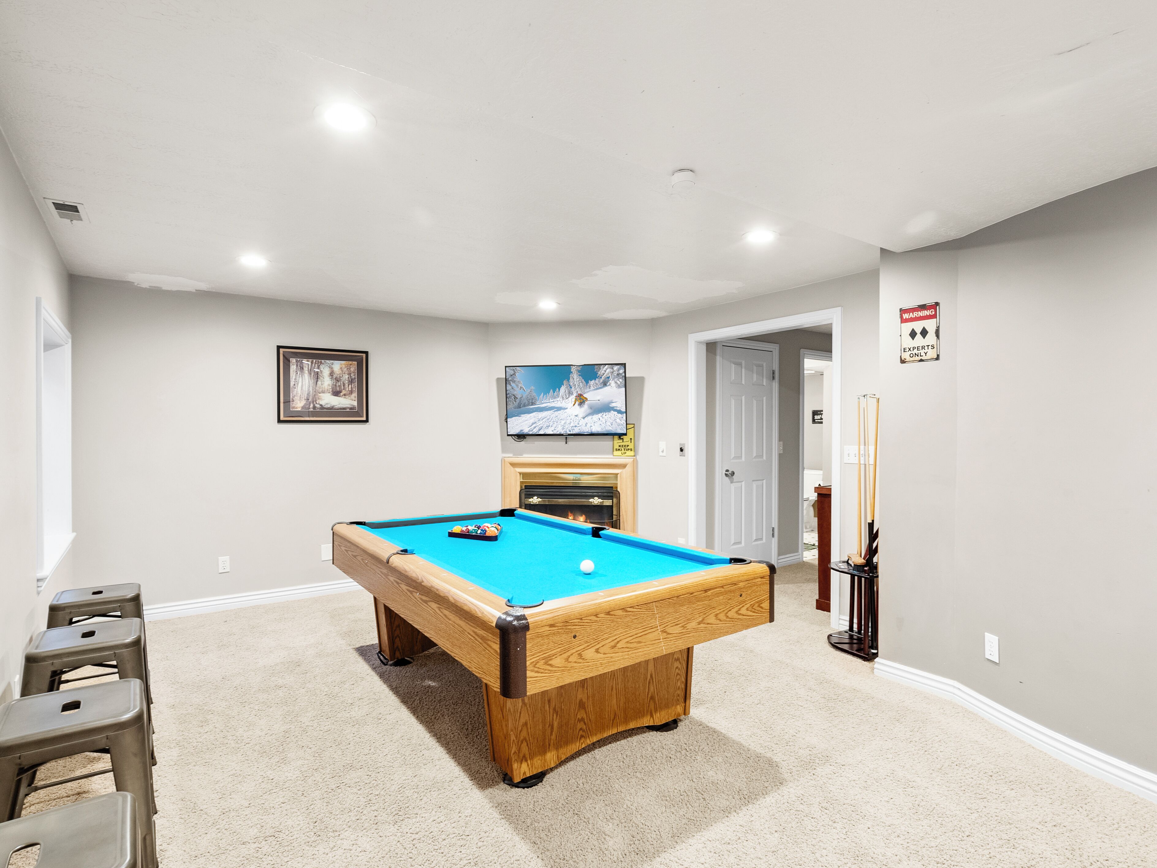 A pool table in a room with a fireplace, a warning sign, and a door leading to another room.
