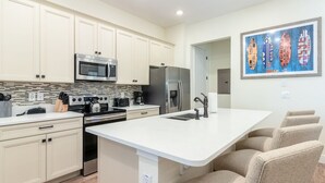 A modern kitchen with white cabinets, stainless steel appliances, a large island with seating, and a tiled backsplash. - Idyllic Waterfront Margaritaville Cottage w/ Private Pool & Spa (Kissimmee)