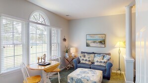 A cozy living room with a blue sofa, a wooden table, and a white chair. There is a painting on the wall and a lamp on a side table. - CH3509, Golf Course Escape, Your Ideal Vacation Home (Sunset Beach)