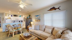 A living room with a beige sofa, a dining area with wicker chairs, a ceiling fan, and a kitchen with white cabinets. - CH3509, Golf Course Escape, Your Ideal Vacation Home (Sunset Beach)