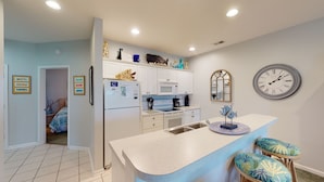 A modern kitchen with white cabinets, a microwave, and a sink. There are decorative items on the counter and a clock on the wall. - CH3509, Golf Course Escape, Your Ideal Vacation Home (Sunset Beach)