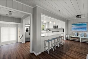 A modern kitchen with white cabinetry, a central island with stools, and pendant lighting. - Beach Break, 4 BR Luxury Home with Gorgeous Ocean Front Views and Private Swimming Pool (North Myrtle Beach)