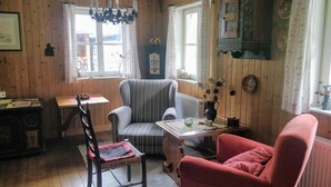 A cozy room with wooden walls, a chandelier, a red armchair, a striped armchair, a wooden table with a vase, and a radiator. - Apartment "ERHOLUNG" for max. 7 persons (2191170) (St. Veit im Defereggental)