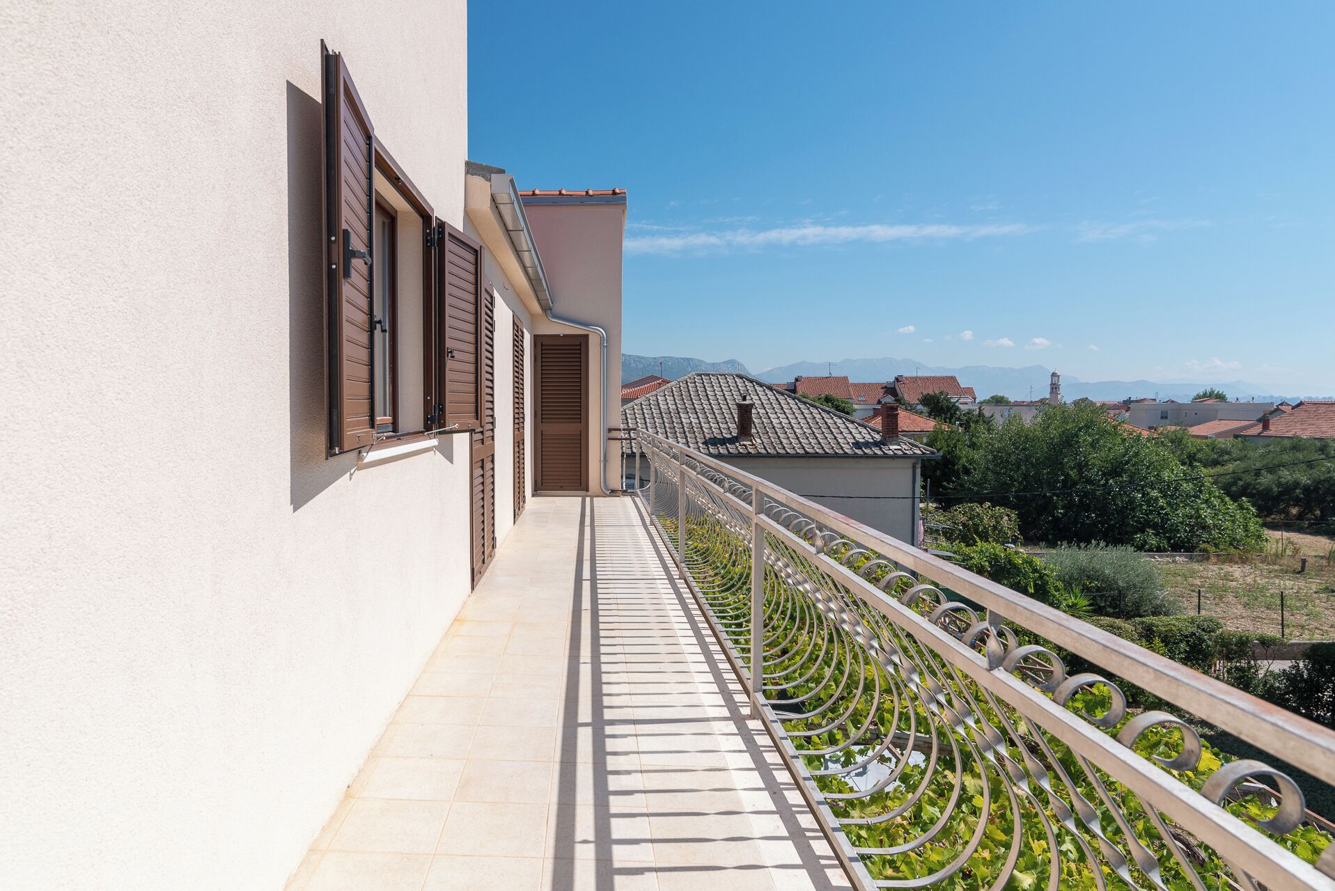 A balcony with a metal railing and a view of a town with red-roofed buildings and mountains in the distance.