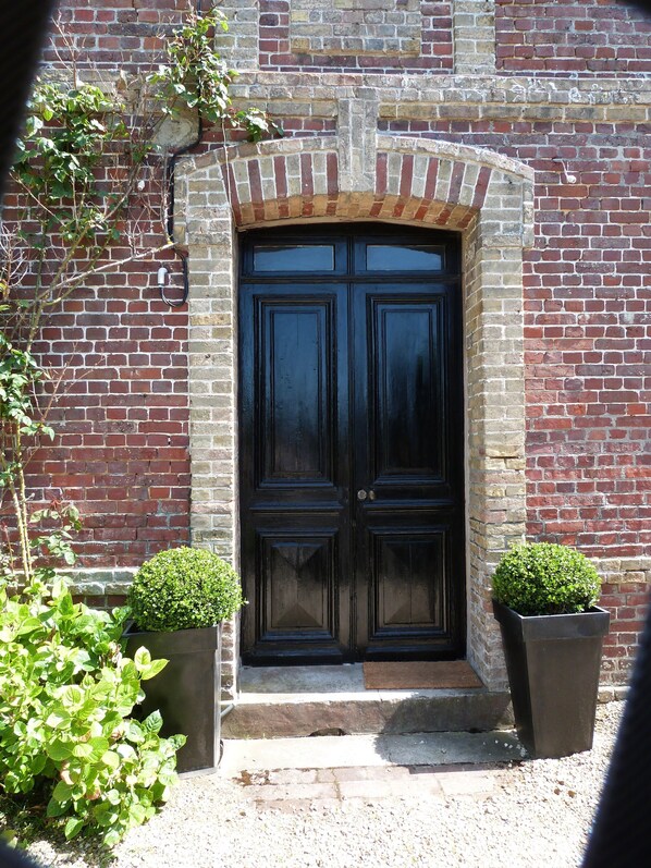 A black double door with a brick archway, flanked by two square planters with green shrubs.