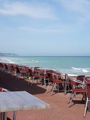 A beachside seating area with red wicker chairs and tables, overlooking the ocean.