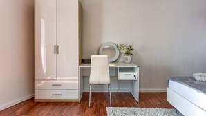 Un dormitorio con una cama, un armario blanco, un escritorio con una silla y un espejo.
