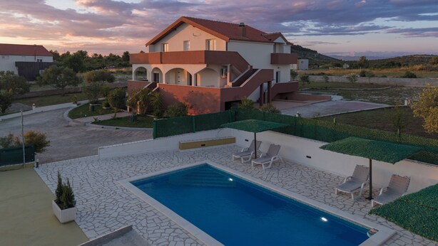 Una casa moderna de dos pisos con piscina, mobiliario exterior y jardín ajardinado.
