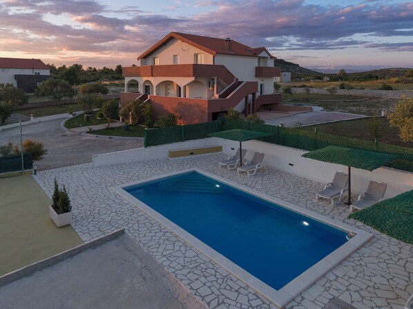 A modern two-story house with a swimming pool, outdoor seating, and a landscaped garden.