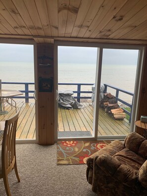 A wooden deck with a view of the sea, a covered seating area, and a large window.