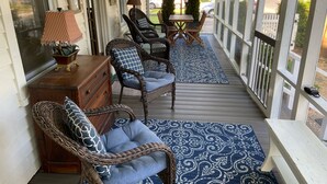Un portico coperto con mobili in vimini, un tavolo in legno e un tappeto blu decorato.