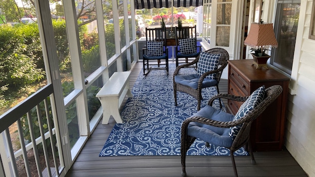Un portico coperto con un tappeto azzurro decorato, sedie in vimini, una panca di legno e un tavolo.