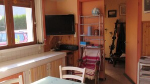 A kitchen with a dining table, chairs, a TV mounted on the wall, and a window overlooking a parking area. - Cottage 4 pers Laruns (Laruns)