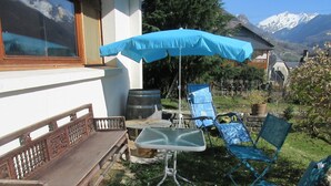 A patio with a wooden bench, a table, and two blue lawn chairs under a blue umbrella. - Cottage 4 pers Laruns (Laruns)