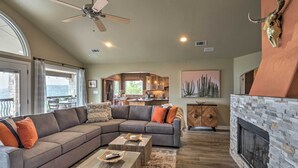 A spacious living room with a sectional sofa, a fireplace, and a view of the kitchen. - Deck & Lake Travis Views: Hill Country Hideaway! (Jonestown)