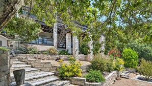A stone staircase leading to a building with a balcony, surrounded by various plants and shrubs. - Deck & Lake Travis Views: Hill Country Hideaway! (Jonestown)