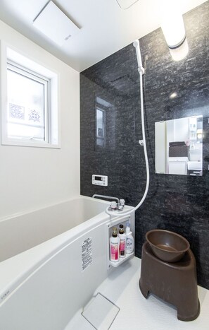 A modern bathroom with a bathtub, a large mirror, and a vanity with toiletries. - Cocomosu Kaigandori (Sumoto)