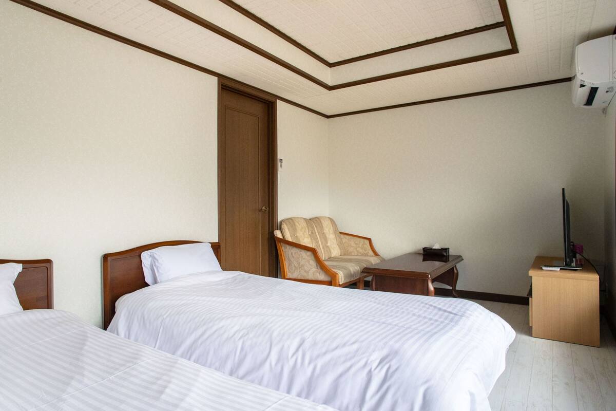 A hotel room with two beds, a chair, a desk, and a TV.