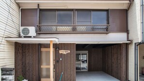 Een gebouw met twee verdiepingen, een overdekte ingang, een houten omheining en een airconditioner.