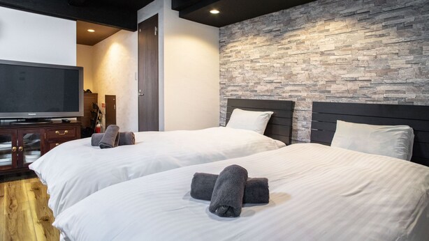 Hotelkamer met twee bedden, een flatscreen televisie, een houten kast en een wand met steenstructuur.