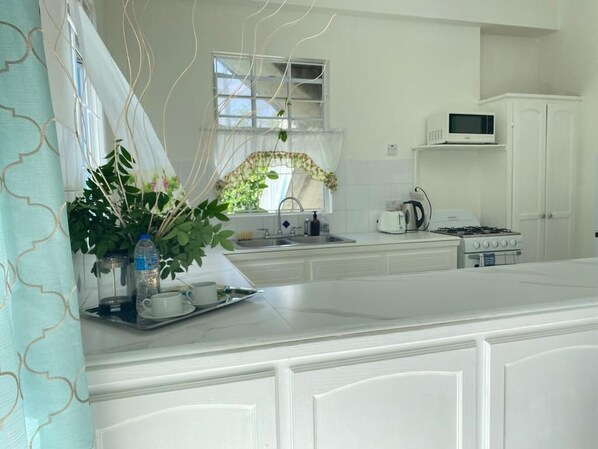 A kitchen with white cabinetry, a microwave, a stove, and a sink. - Cozy Apartments close to beach, bars and restaurants (Rodney Bay)